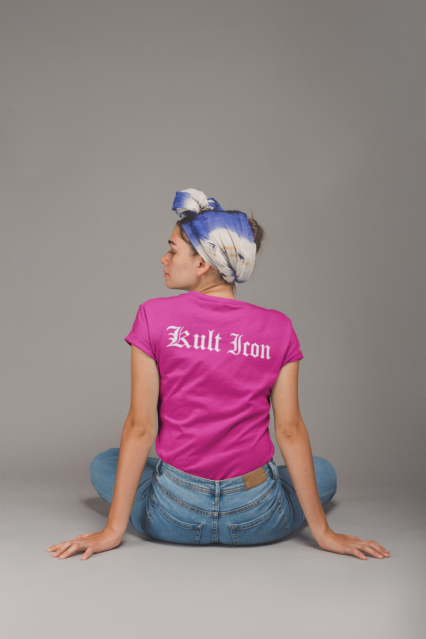 Person wearing a pink 'Kult Iron' t-shirt sitting on the floor with a gray background