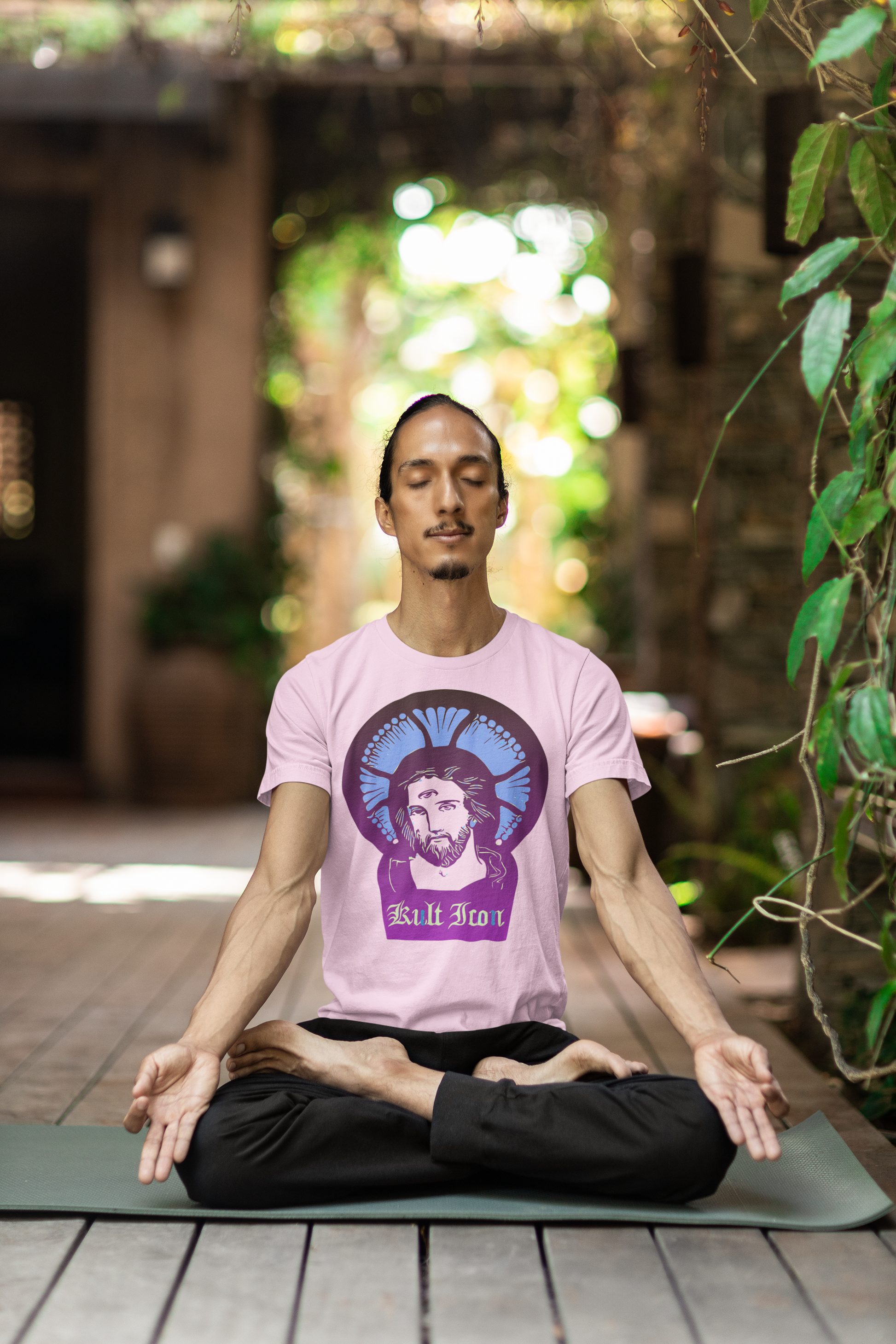 Man meditating on a mat wearing a pink t-shirt with a graphic design.