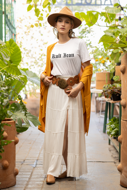 Woman in a white outfit with a yellow cardigan and hat, standing in a garden.