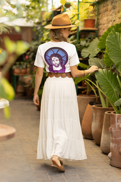 Woman in a garden wearing a white t-shirt with a graphic design and a white skirt.