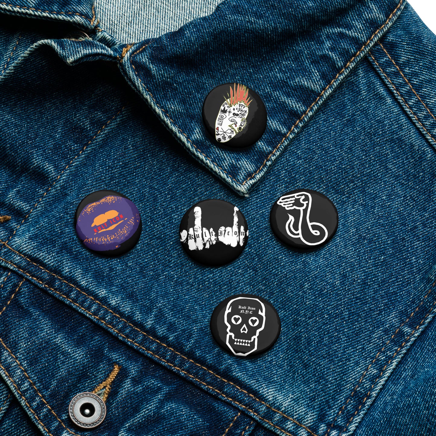 Five pins on a denim jacket with various designs.