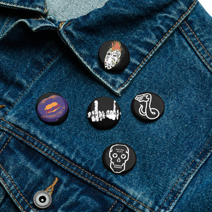 Five pins on a denim jacket with various designs.